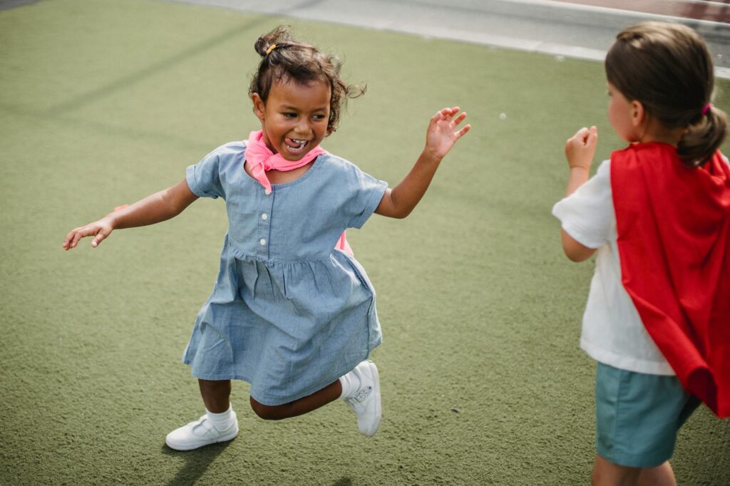 Two young children wearing capes play joyfully outdoors, expressing fun and imagination.